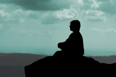 Silhouette man standing on rock against sky