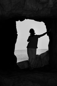 Silhouette of a young woman standing on a hole in the rock against the sky during sunset