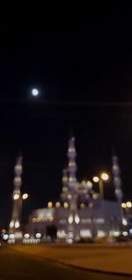Defocused image of illuminated city street against sky at night