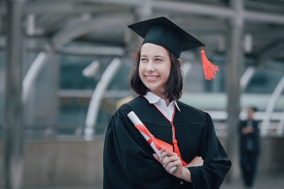 Smiling young woman in graduation gown standing outdoors