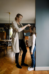 Full length of mother measuring daughter's height against wall at home