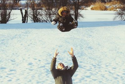 Smiling young man throwing son in mid-air on snow covered field