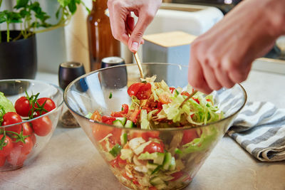 Woman mixing green vegetable salad in bowl at kitchen