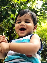 Portrait of smiling baby boy sitting against tree