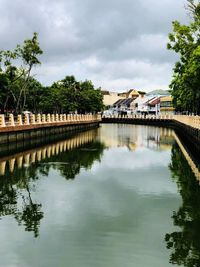 Bridge over lake by buildings against sky