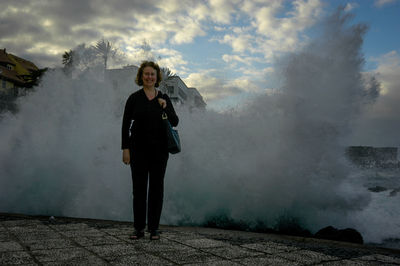 Full length portrait of young woman standing against sky