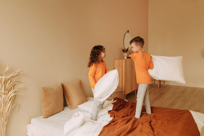 Funny happy kids brother and sister in pajamas playing fighting with pillows in cozy bedroom at home
