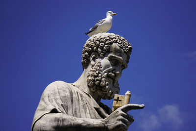 Low angle view of seagull perching on statue against blue sky