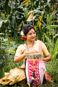 Smiling young woman playing musical instrument while sitting on grassy field