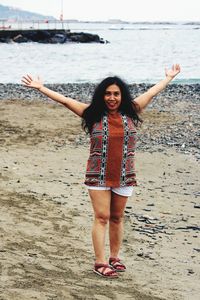 Portrait of happy mature woman with arms outstretched standing at beach