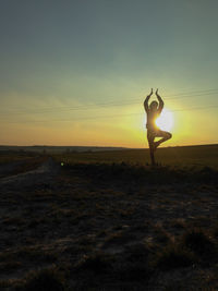 Woman practicing tree pose yoga on field during sunrise