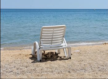 Empty chairs on beach by sea against sky