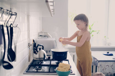 Cute toddler child in kitchen by stove helps mom cook, bright interior of kitchen