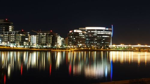 Illuminated buildings by river against clear sky at night