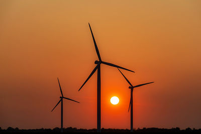 Silhouette wind turbines on field against orange sky