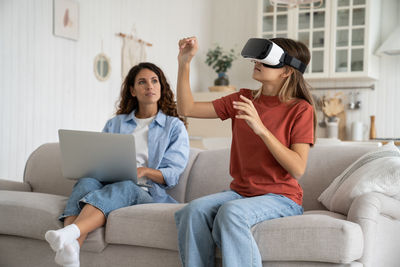 Curious teen girl using vr headset for study while mother working remotely on laptop