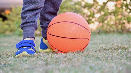 Low section of boy standing by basketball on field