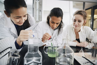 Mature chemistry teacher looking at young university student mixing liquid solution in beaker