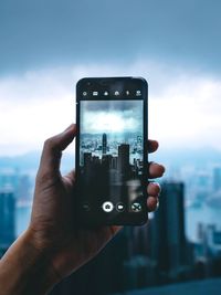 Midsection of person holding smart phone against sky
