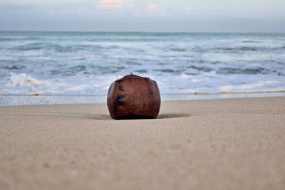 Stone ball on sand at beach against sky