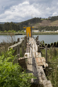 Wooden posts on field by river against sky
