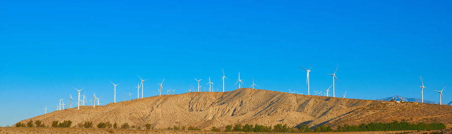 Wind turbines on land against clear blue sky