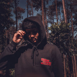 Portrait of young man standing against trees