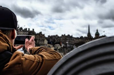 Cropped image of man photographing city through mobile phone