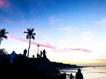 Silhouette people by palm trees against sky during sunset