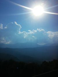 Sun shining through clouds over mountains