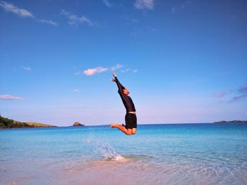 Man jumping on shore at beach against sky
