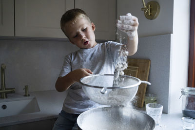 Cute boy sieving flour for cake preparation at home