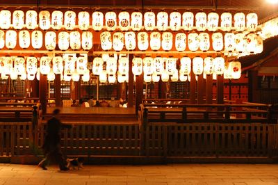 Man walking on illuminated street amidst buildings in city