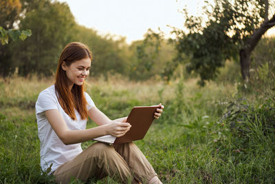 Young woman using laptop while sitting on field