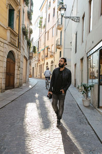 Full length of young man walking on street amidst buildings