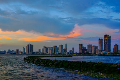 Sea by buildings against sky during sunset