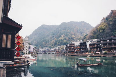 Boats in river by buildings against sky