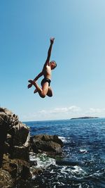 Low angle view of man jumping over sea against clear sky