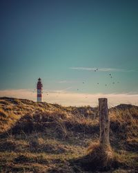 Lighthouse on field by buildings against sky