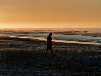 Silhouette man walking at beach against clear sky during sunset