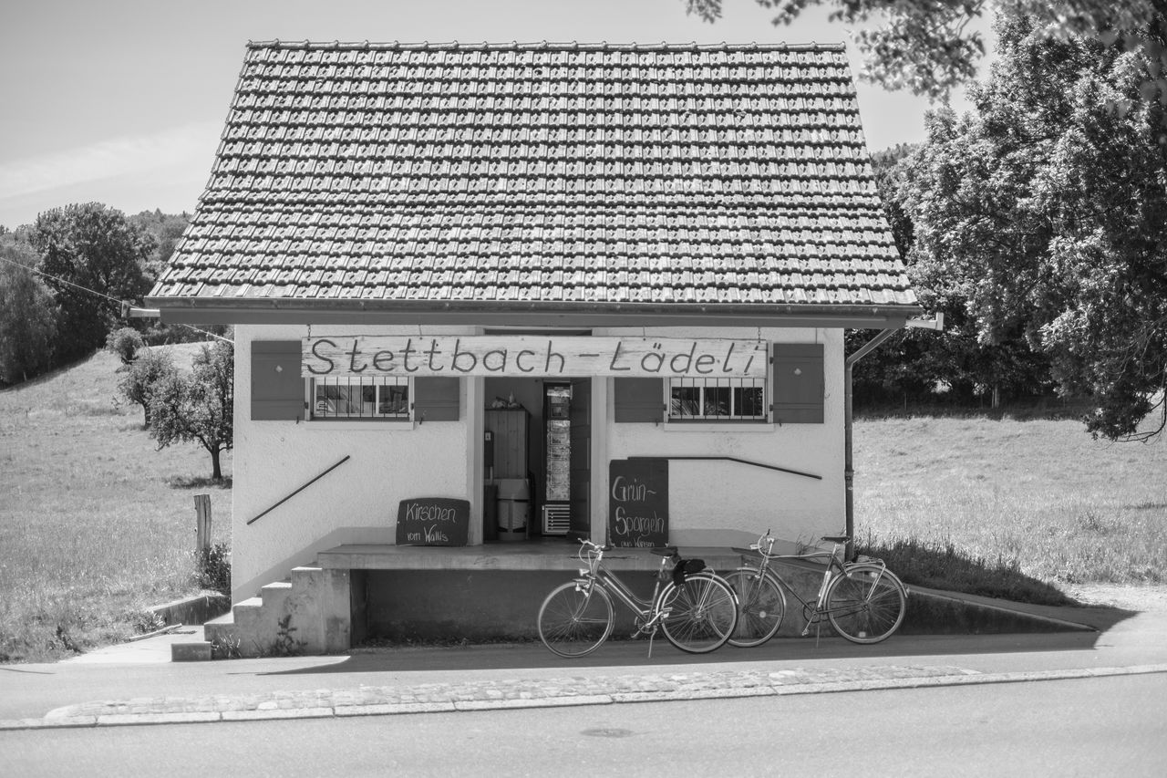 black and white, architecture, built structure, building exterior, monochrome photography, text, monochrome, house, plant, tree, land vehicle, history, day, transportation, nature, vehicle, bicycle, no people, western script, building, home, communication, outdoors, wheel, white