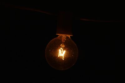 Close-up of light bulb hanging against black background