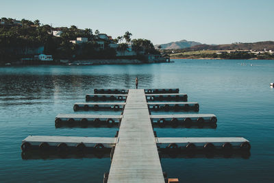 Woman standing on pier in lake against clear sky