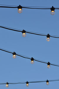 Strings of illuminated electric light bulbs outdoors against blue sky