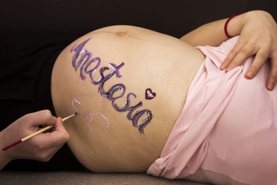 Cropped hand of man making painting on pregnant woman belly