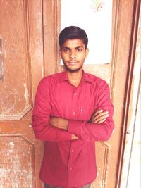 Portrait of young man standing against door at home