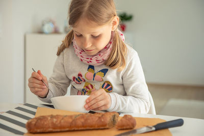 Girl having breakfast with bread while sitting on table