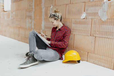 Woman working while sitting against wall