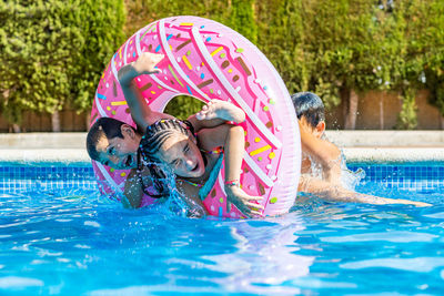 Three kids playing with a rubber ring into a pool