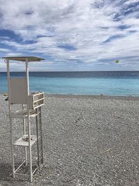 Empty life guard/bay watch chairs on beach against sky